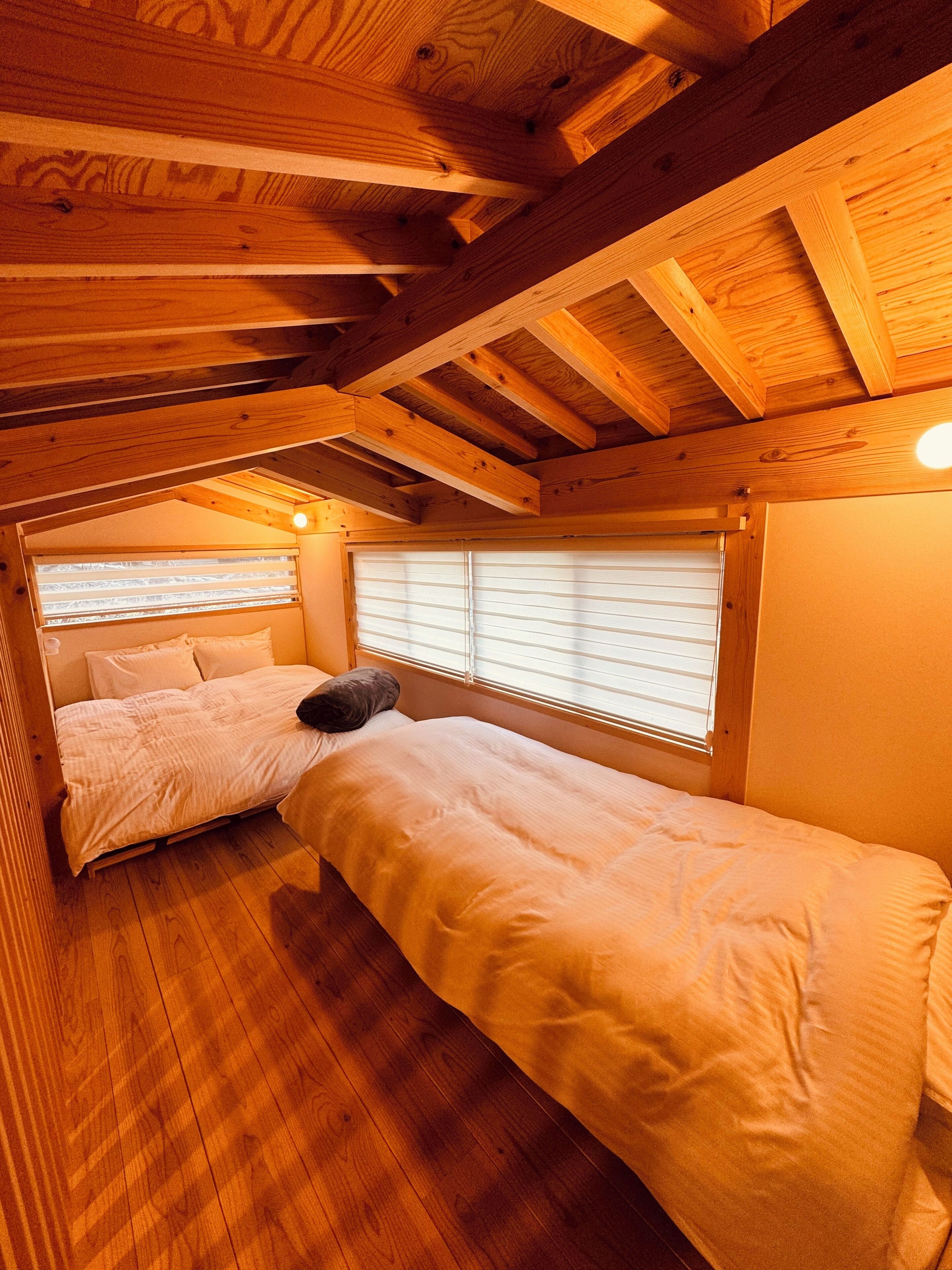 Une chambre confortable avec un lit en mezzanine, un lit plus petit et une fenêtre avec des stores.