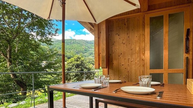 An outdoor wooden deck with a table set for two, a bench, and a large umbrella. - CrossFit Otoyo Strength TINY HOUSE (Otoyo)