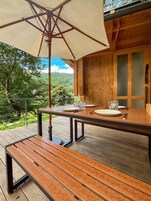 Una terraza de madera al aire libre con una mesa preparada para dos personas, un banco y un paraguas grande.