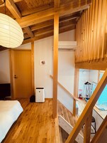 Un interior de madera con una cama, un cubo de basura y una escalera.