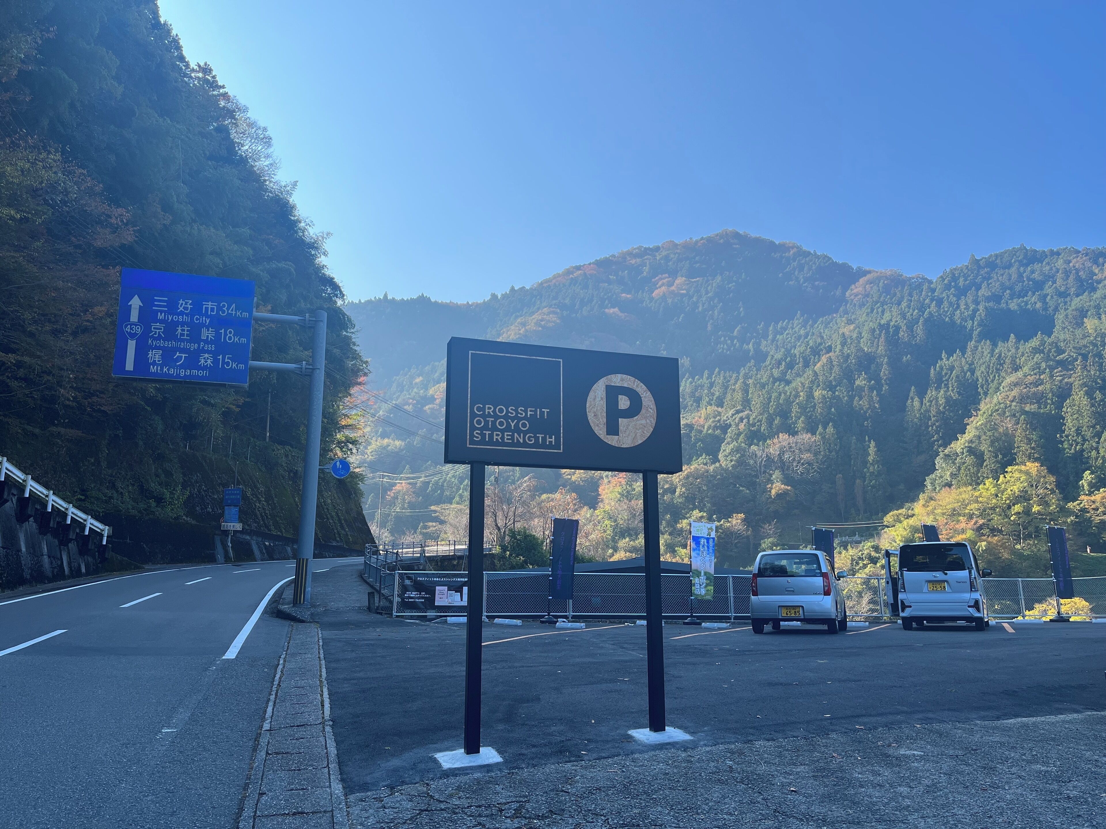 Ein Parkplatzschild mit dem Buchstaben 'P', ein blaues Hinweisschild und eine Berglandschaft im Hintergrund.