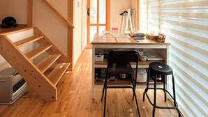 A wooden interior with a staircase, a desk with chairs, and a window with blinds. - CrossFit Otoyo Strength TINY HOUSE (Otoyo)