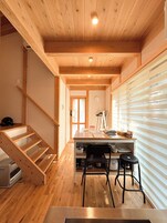 Un interior de madera con una escalera, un escritorio con sillas y un ventanal con persianas.