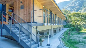 A modern building with a wooden exterior, concrete steps, and a balcony overlooking a mountainous landscape. - CrossFit Otoyo Strength TINY HOUSE (Otoyo)