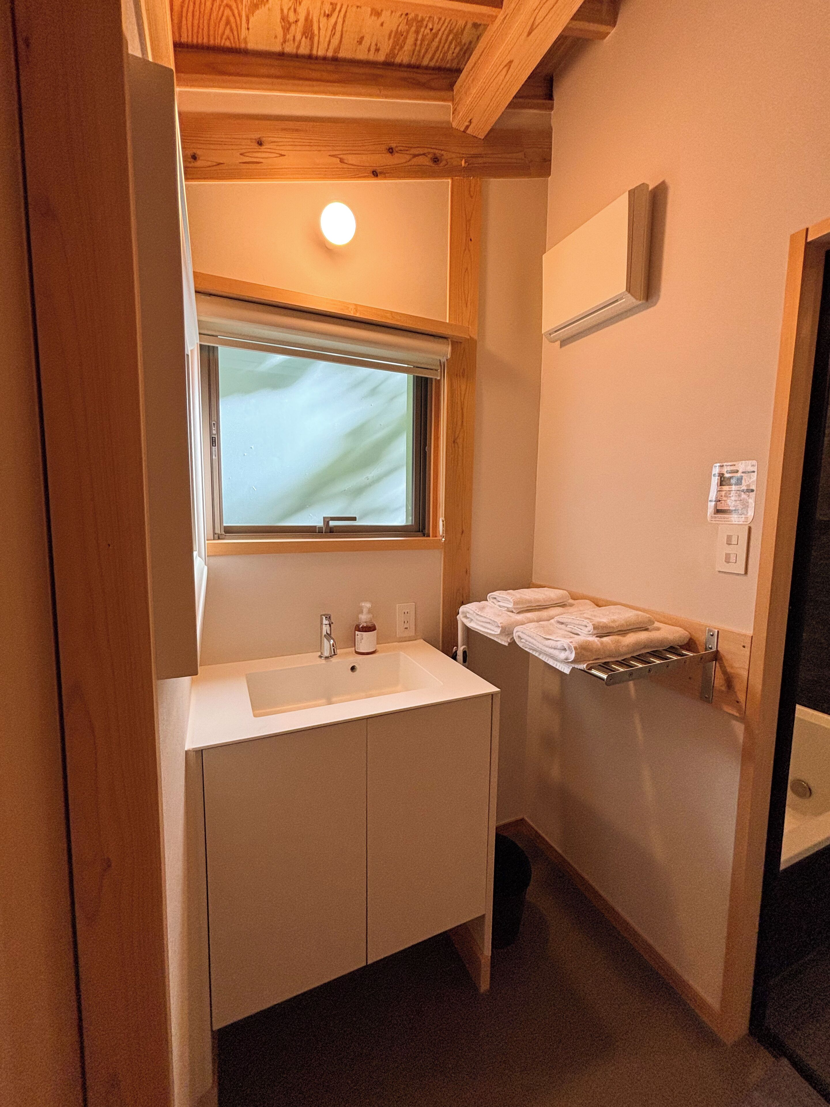 A compact bathroom with a white sink, a window above the mirror, and a towel rack.
