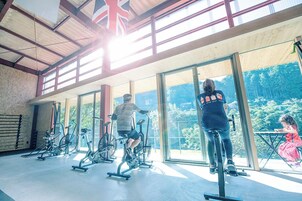 Un gimnasio con bicicletas estáticas y un amplio ventanal con vista a un área boscosa.