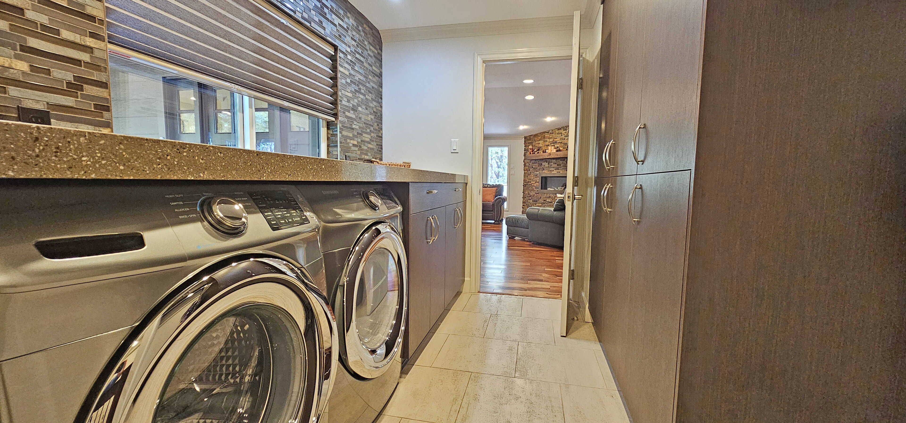 A laundry area with a washing machine and dryer, a kitchen with a granite countertop, and a hallway leading to a living room with a sofa and a fireplace.