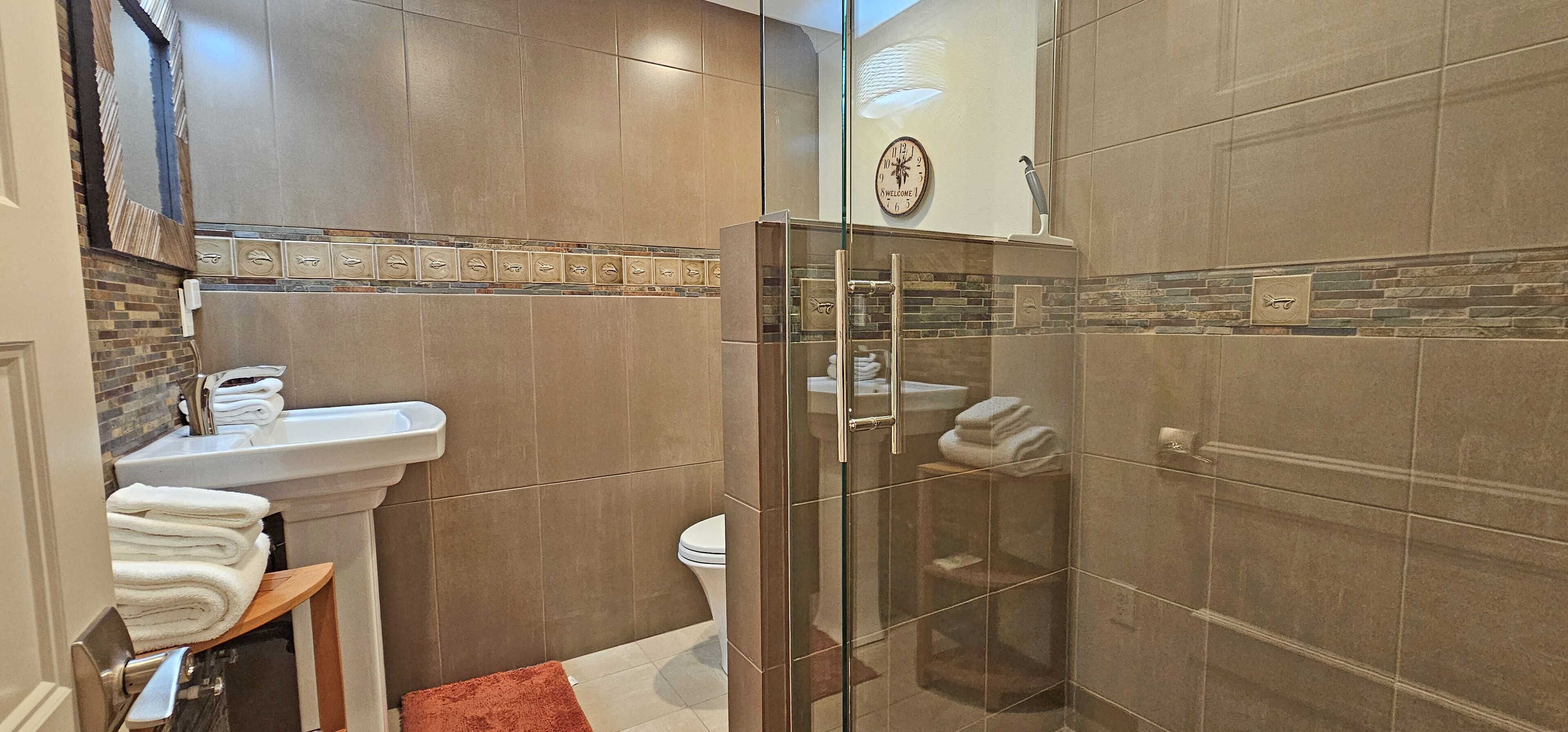 Un baño con ducha de vidrio, lavamanos con espejo e inodoro.