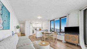 A modern apartment with a living room, dining area, kitchen, and a large window offering a city view.