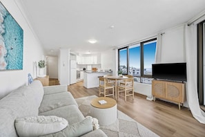 A modern apartment with a living room, dining area, kitchen, and a large window offering a city view.
