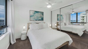 A hotel room with a large bed, a ceiling fan, a large window, and a view of the city.