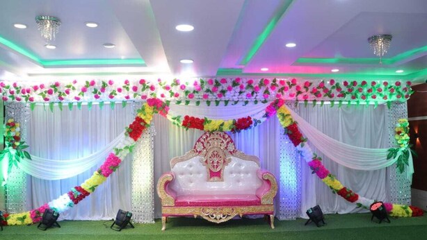 A stage with a white and pink sofa, surrounded by floral decorations and draped fabric. - Royal Park Celebration By GRB (Patna)
