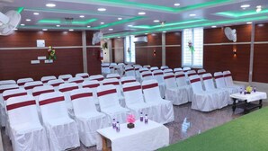 A conference room with rows of white chairs, each with a red sashed backrest, and tables with white tablecloths. - Royal Park Celebration By GRB (Patna)