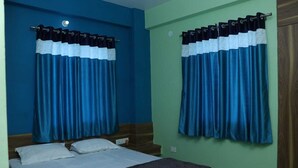 A bedroom with two beds, blue curtains, and a green wall. - Royal Park Celebration By GRB (Patna)