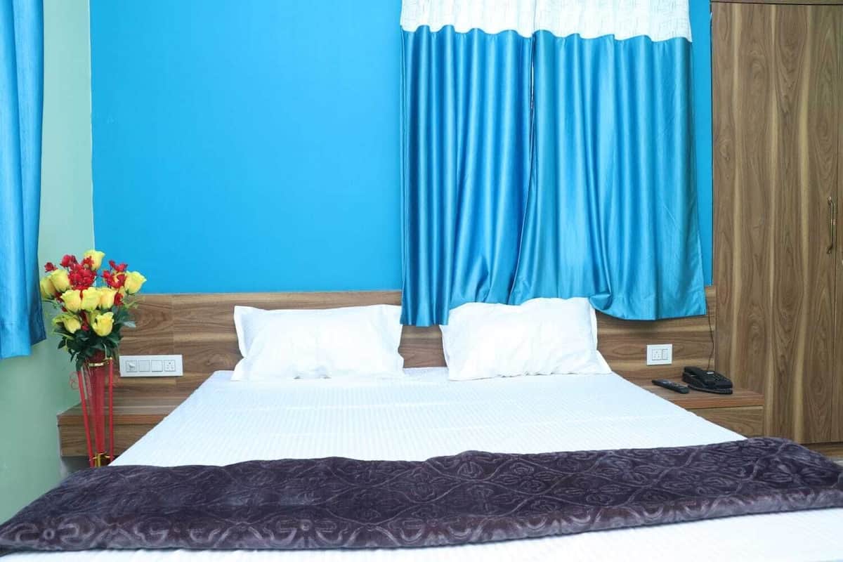 Una habitación de hotel con una cama, dos almohadas, un florero con flores y un armario de madera.