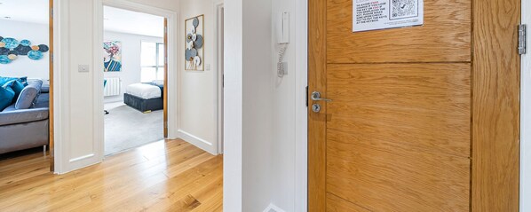 Un couloir avec une porte en bois, un mur blanc et un interphone.