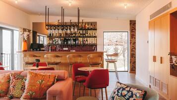 Uma área de bar moderna com diversos frascos de bebidas, um espaço de estar com cadeiras vermelhas e uma grande janela com vista para o exterior.