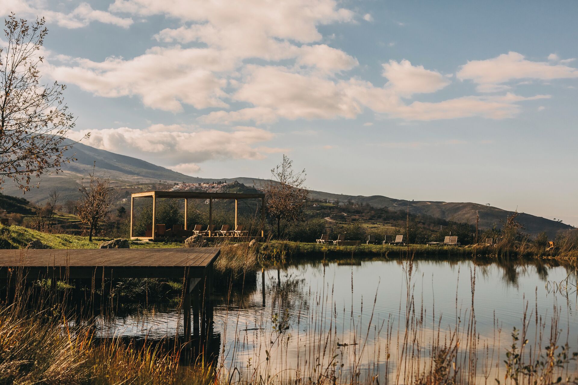 A lakeside pavilion with a view of a mountain range and a small village in the distance.