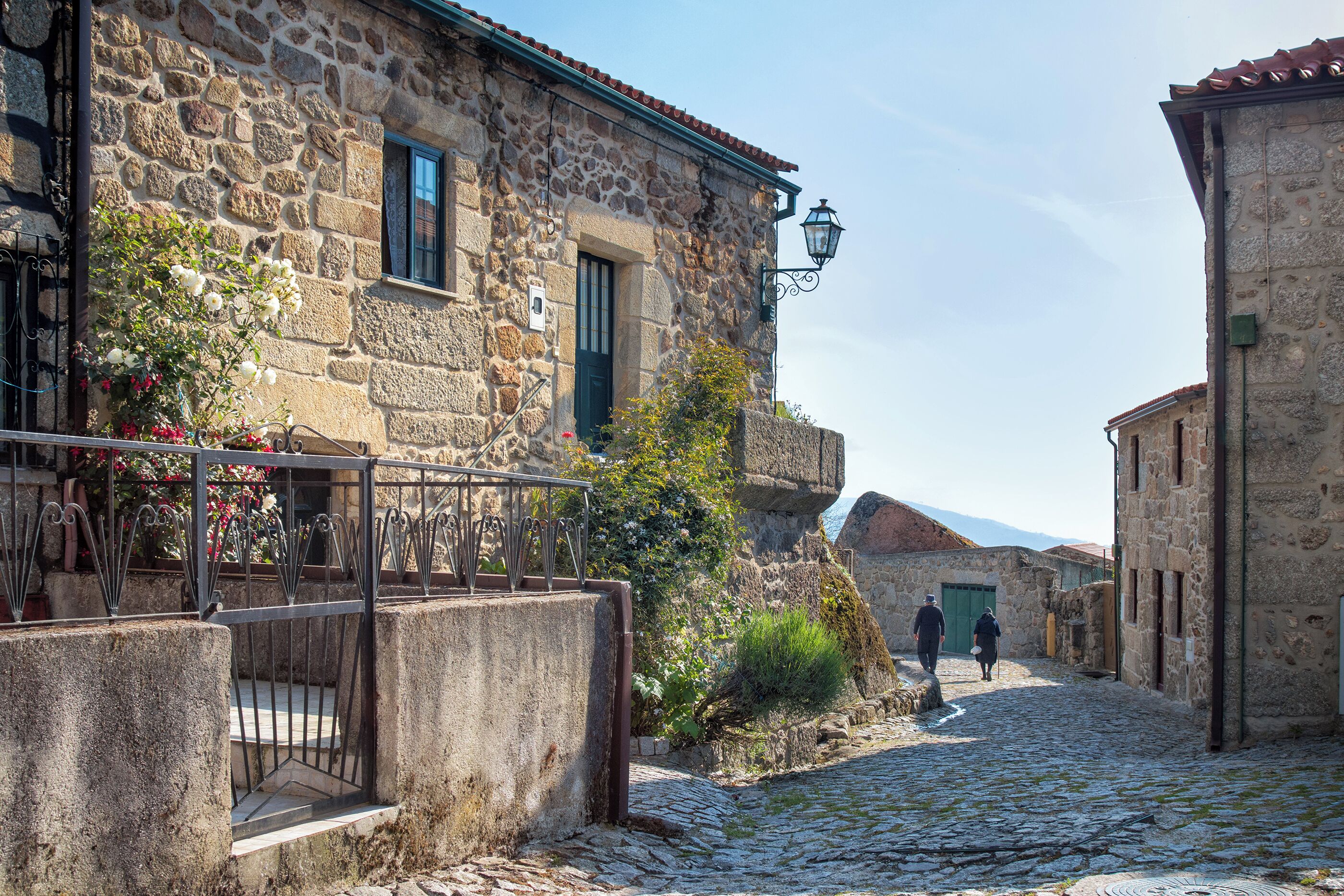 A stone building with a metal gate, a cobblestone street, and a person walking away.