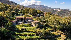 Una propiedad en una ladera con varios edificios de piedra, jardines en terrazas y montañas al fondo.