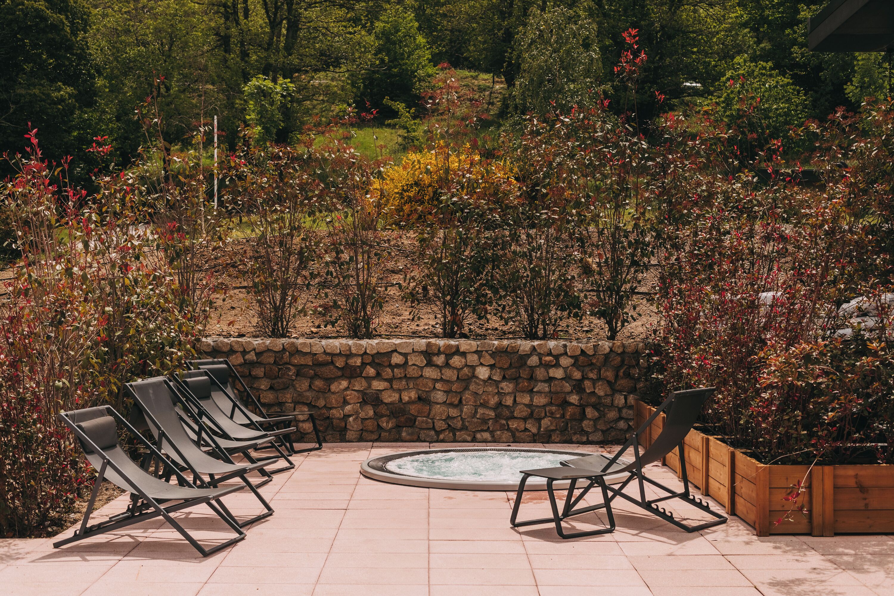 Ein Patio mit Steinmauern, einem Whirlpool und Liegestühlen.