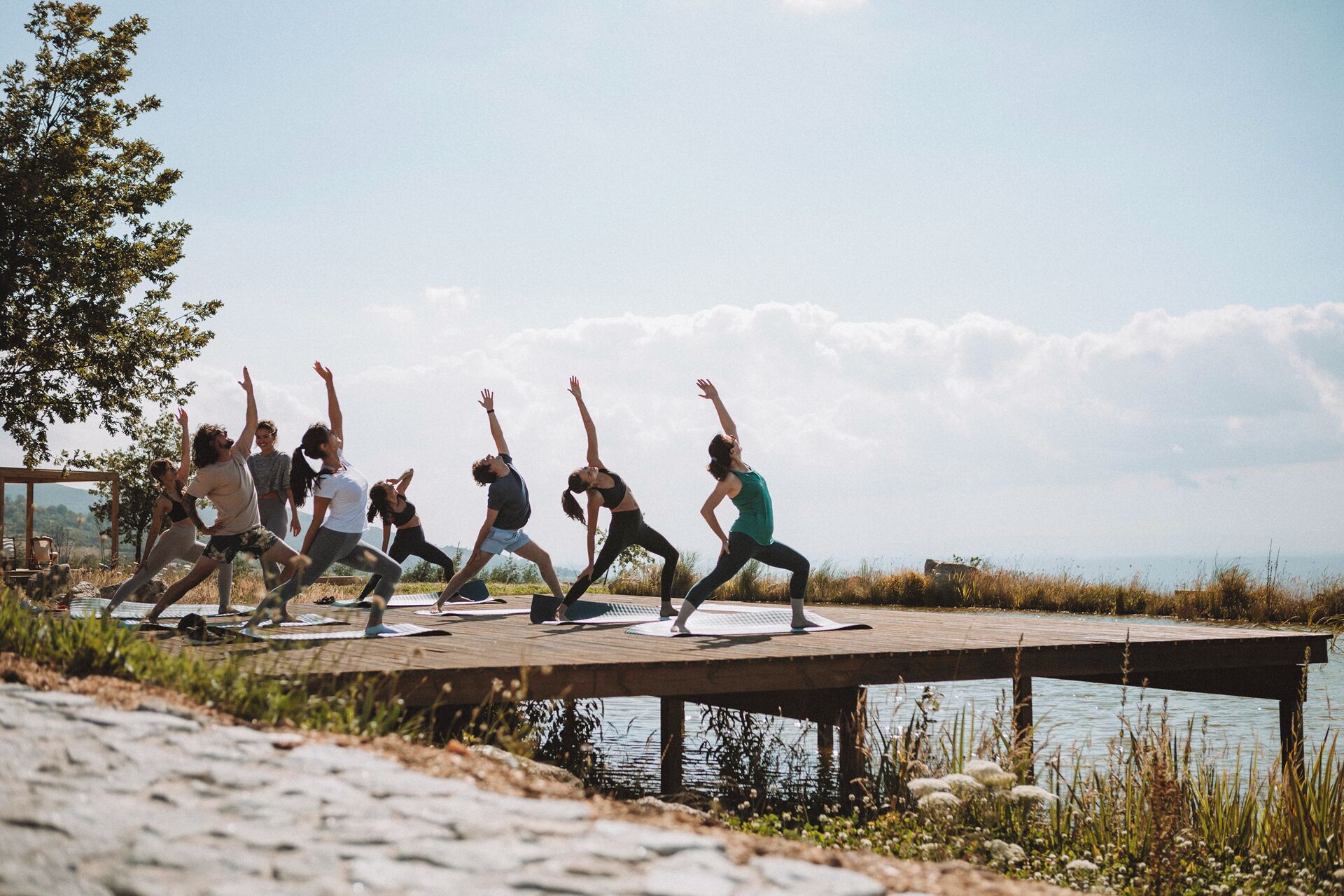 A group of people performing yoga on a wooden dock by a body of water.