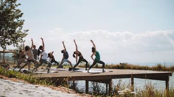 A group of people performing yoga on a wooden dock by a body of water.
