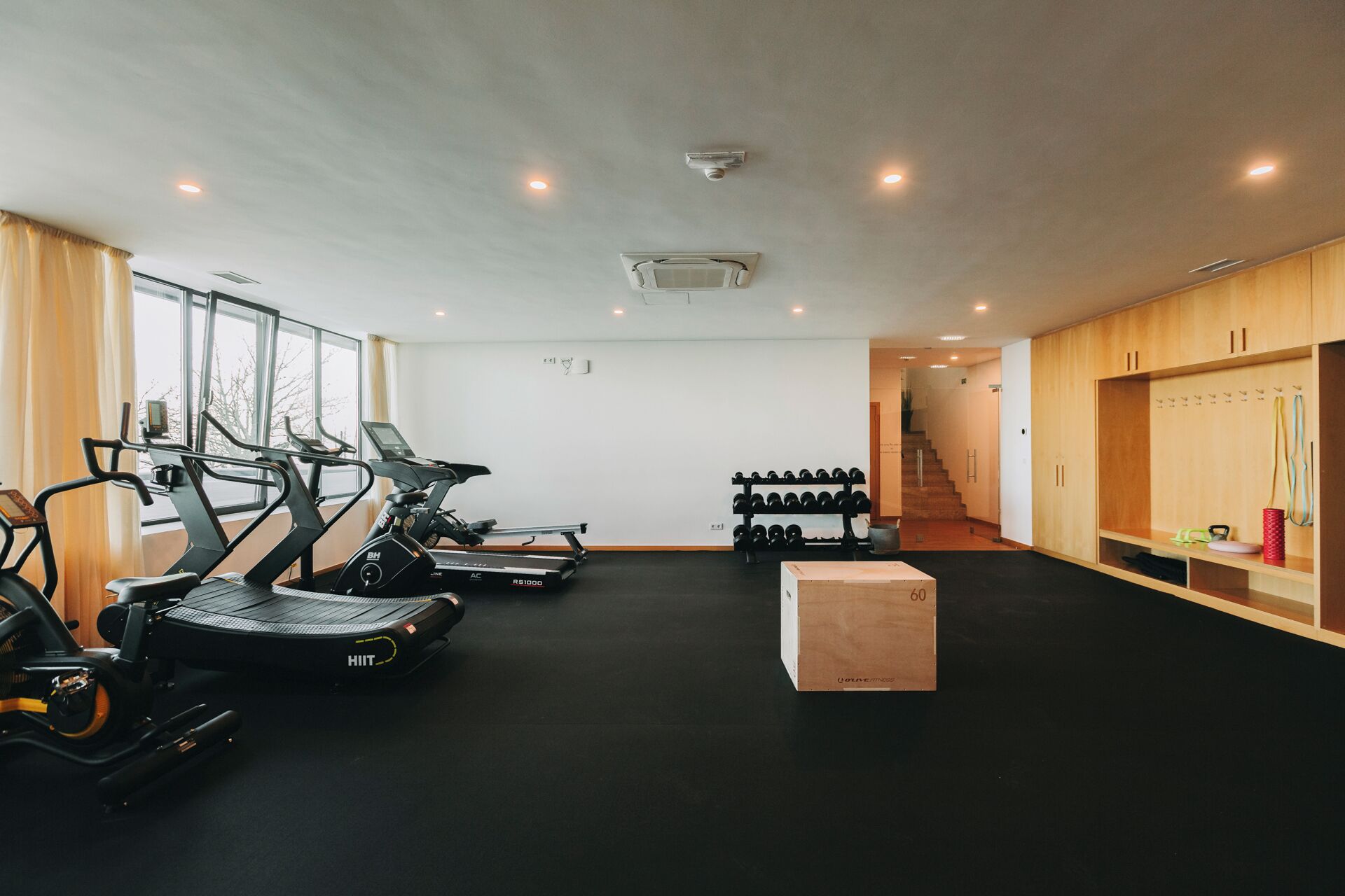 Un gimnasio con cintas de correr, un soporte para pesas y un banco de madera.