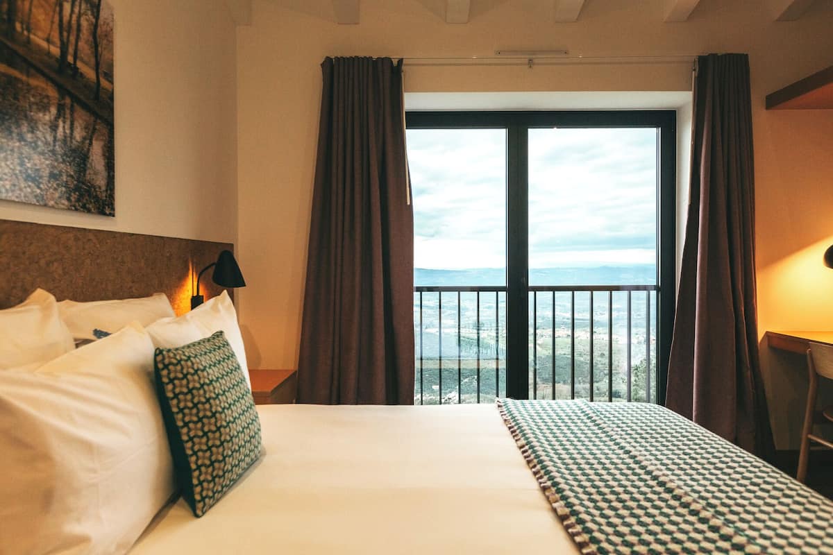 Et hotelværelse med en stor seng, udsigt fra en balkon og et billede på væggen.