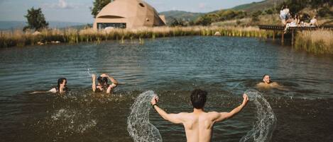 A group of people in a natural water setting with a unique geodesic dome structure in the background.