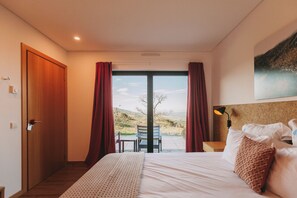 A hotel room with a large bed, a desk, a chair, and a view of the countryside. - Estrela Serenity - Resort (Gouveia)