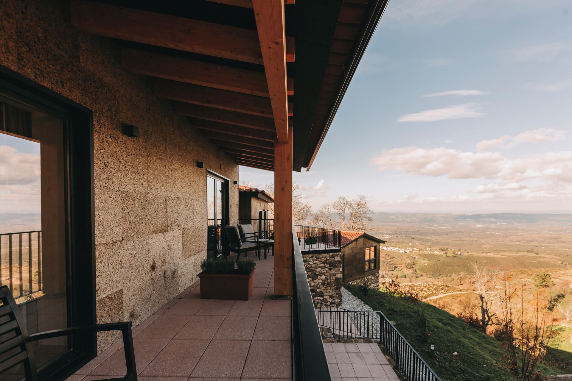 Un espace extérieur abrité, avec vue sur une vallée, agrémenté d’une pergola en bois et d’un coin salon avec des chaises et une table.