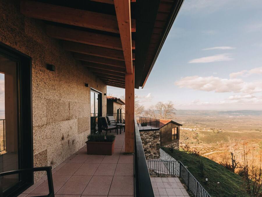 Un espace extérieur abrité, avec vue sur une vallée, agrémenté d’une pergola en bois et d’un coin salon avec des chaises et une table.