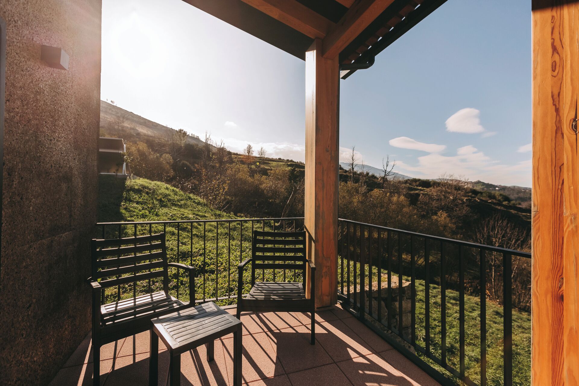 A balcony with two wooden benches and a railing, overlooking a hilly landscape.