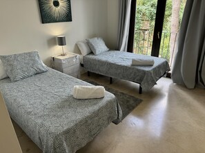 Un dormitorio con dos camas, una mesita de noche, una lámpara y vistas al verdor exterior.