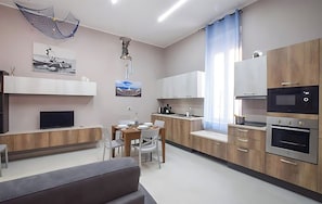 A modern kitchen with wooden cabinets, a dining area with a table and chairs, a TV, and a ceiling light fixture.