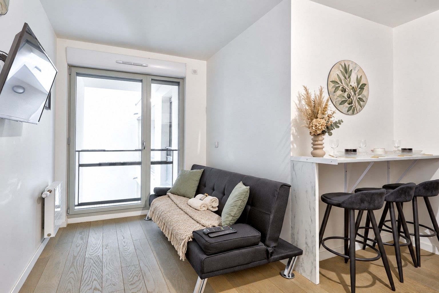 A modern living room with a sofa, a dining area with a table and chairs, and a large window providing natural light.