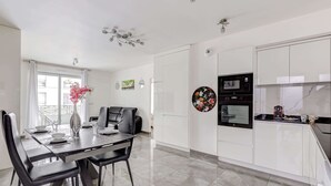 A modern kitchen with white cabinets, a dining area with a glass table and black chairs, and a decorative vase with pink flowers.