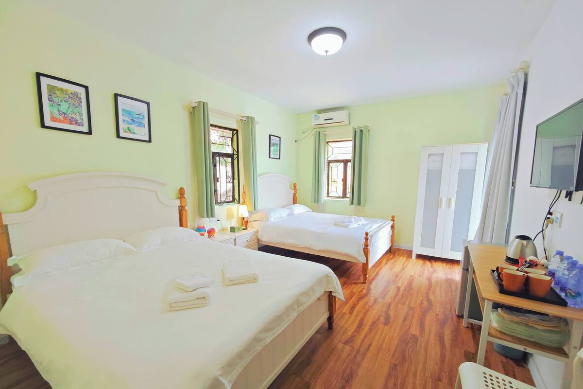 Une chambre d’hôtel avec deux lits, un bureau avec une bouilloire et un téléviseur fixé au mur.