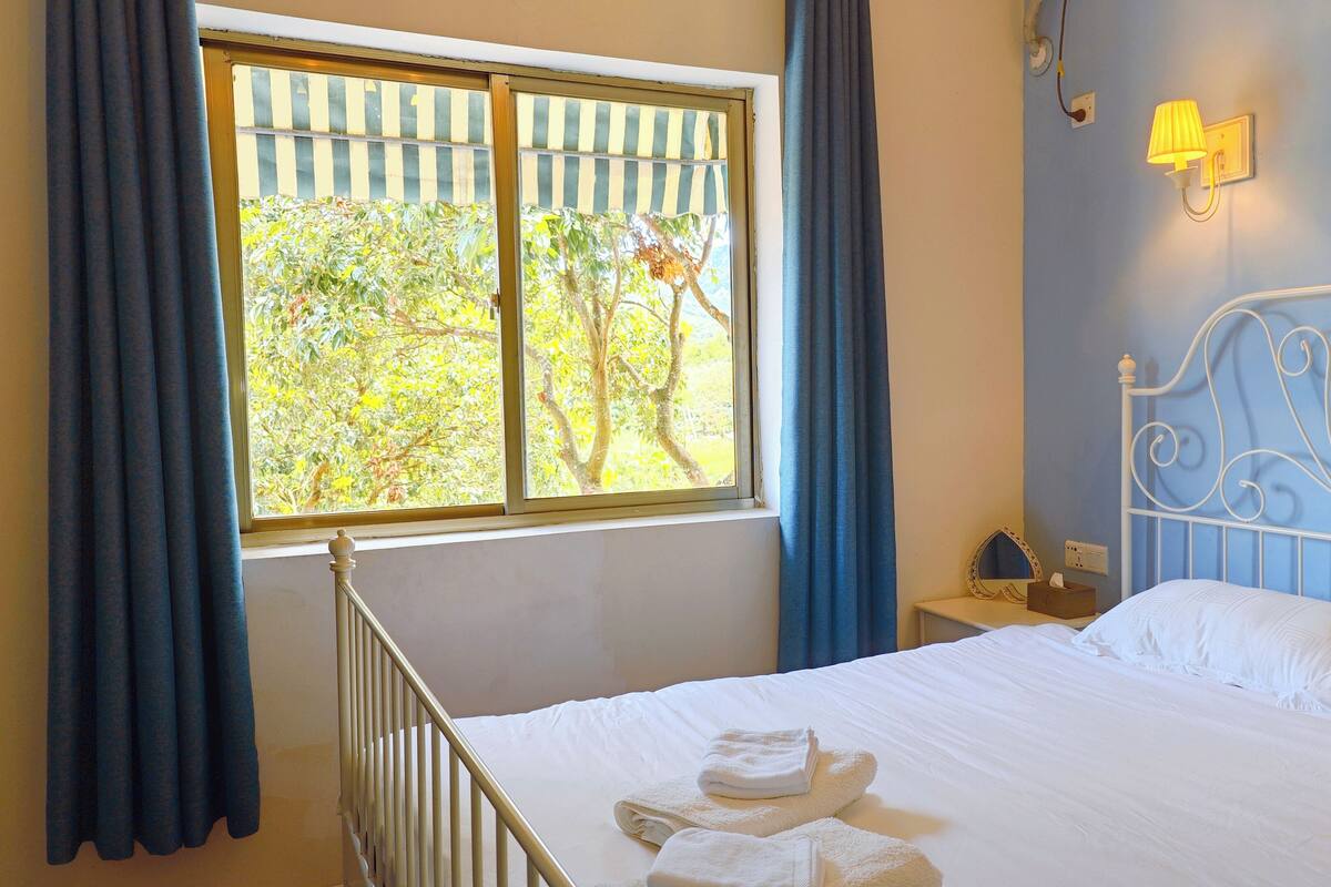 Une chambre à coucher avec un lit, une table de chevet, une lampe et une fenêtre avec des rideaux.