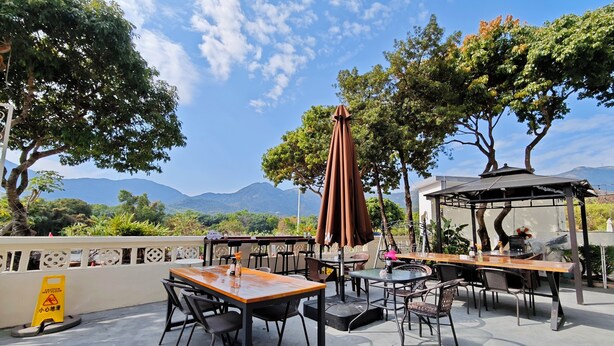 Une terrasse extérieure avec des tables et des chaises, un panneau indiquant un sol glissant, et une vue sur les montagnes.