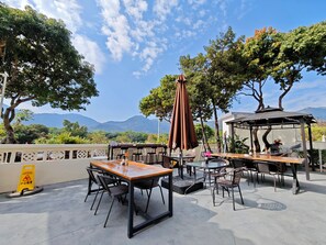 Eine Terrasse im Freien mit Tischen und Stühlen, einem Hinweis auf nassen Boden und Blick auf Berge.