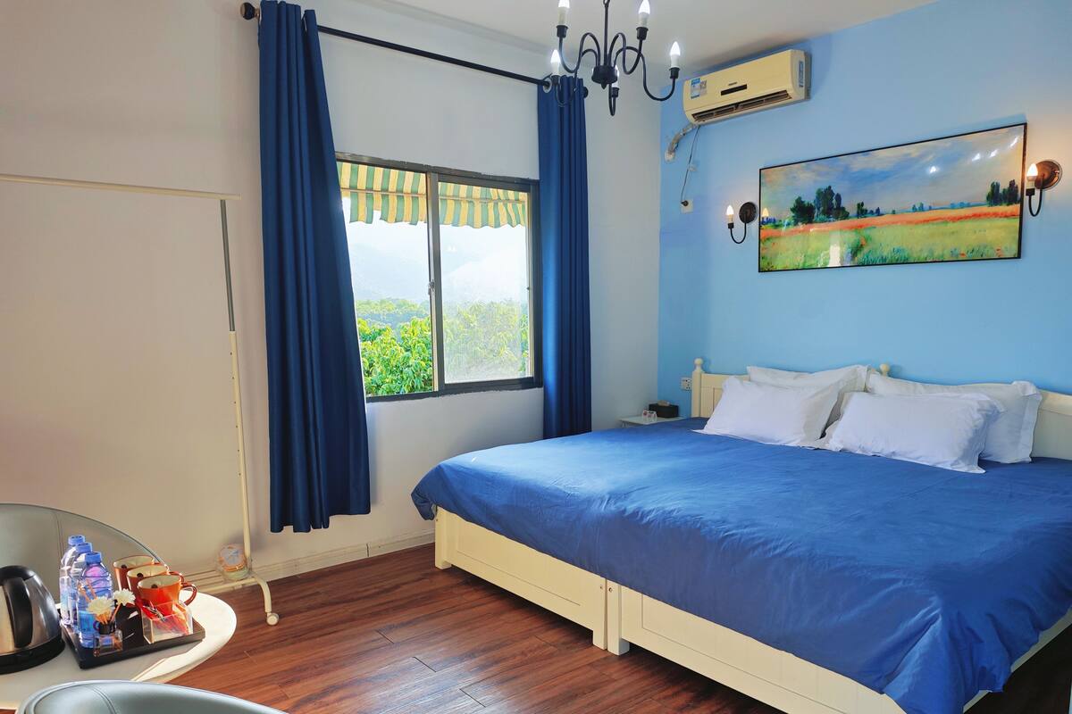 Une chambre à coucher avec un lit, une chaise, un bureau avec une bouilloire, des tasses et une bouteille d’eau.