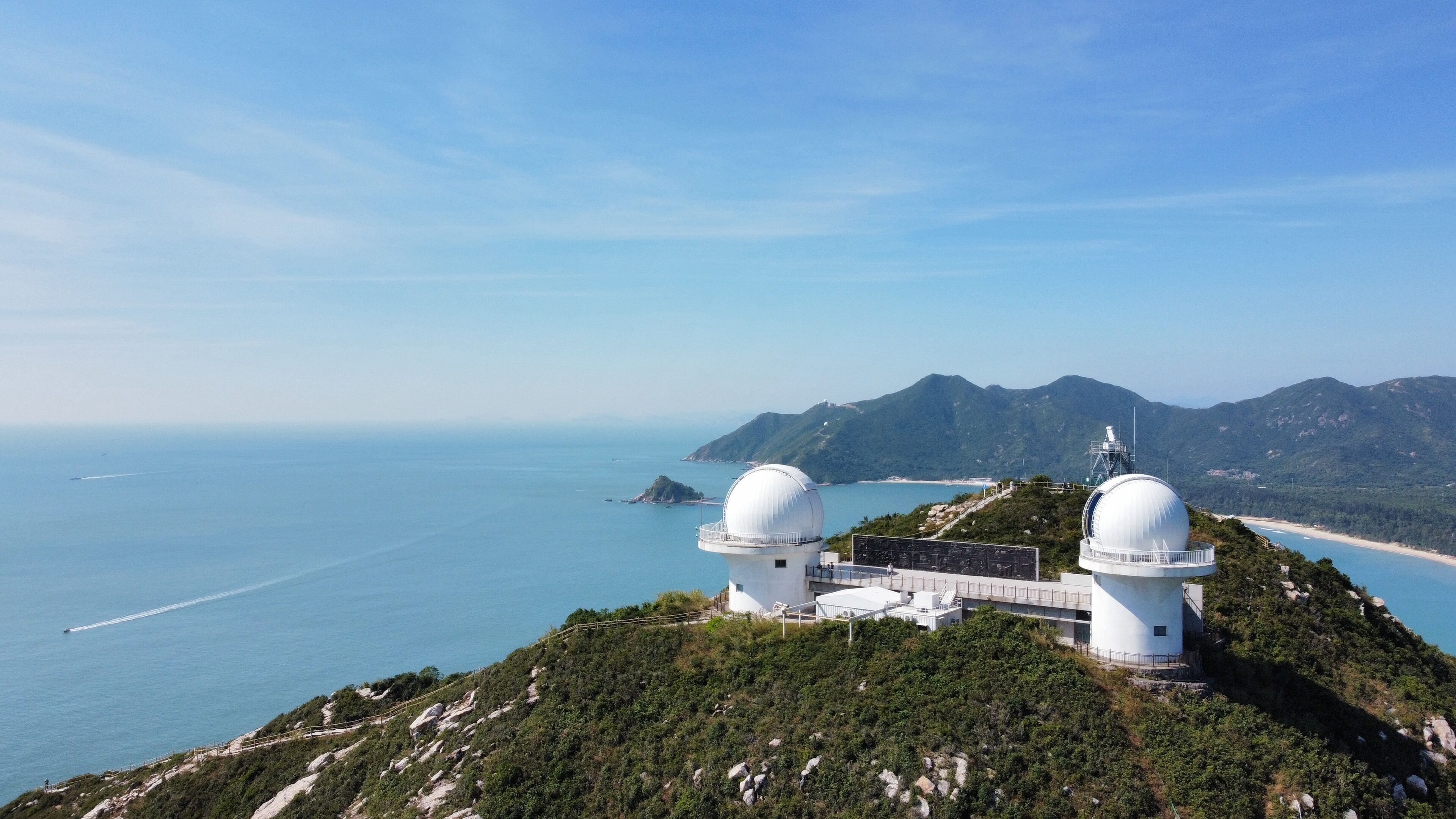 Un observatoire situé sur la côte, doté de deux coupoles, offrant une vue dégagée sur la mer et s’inscrivant dans un paysage montagneux.