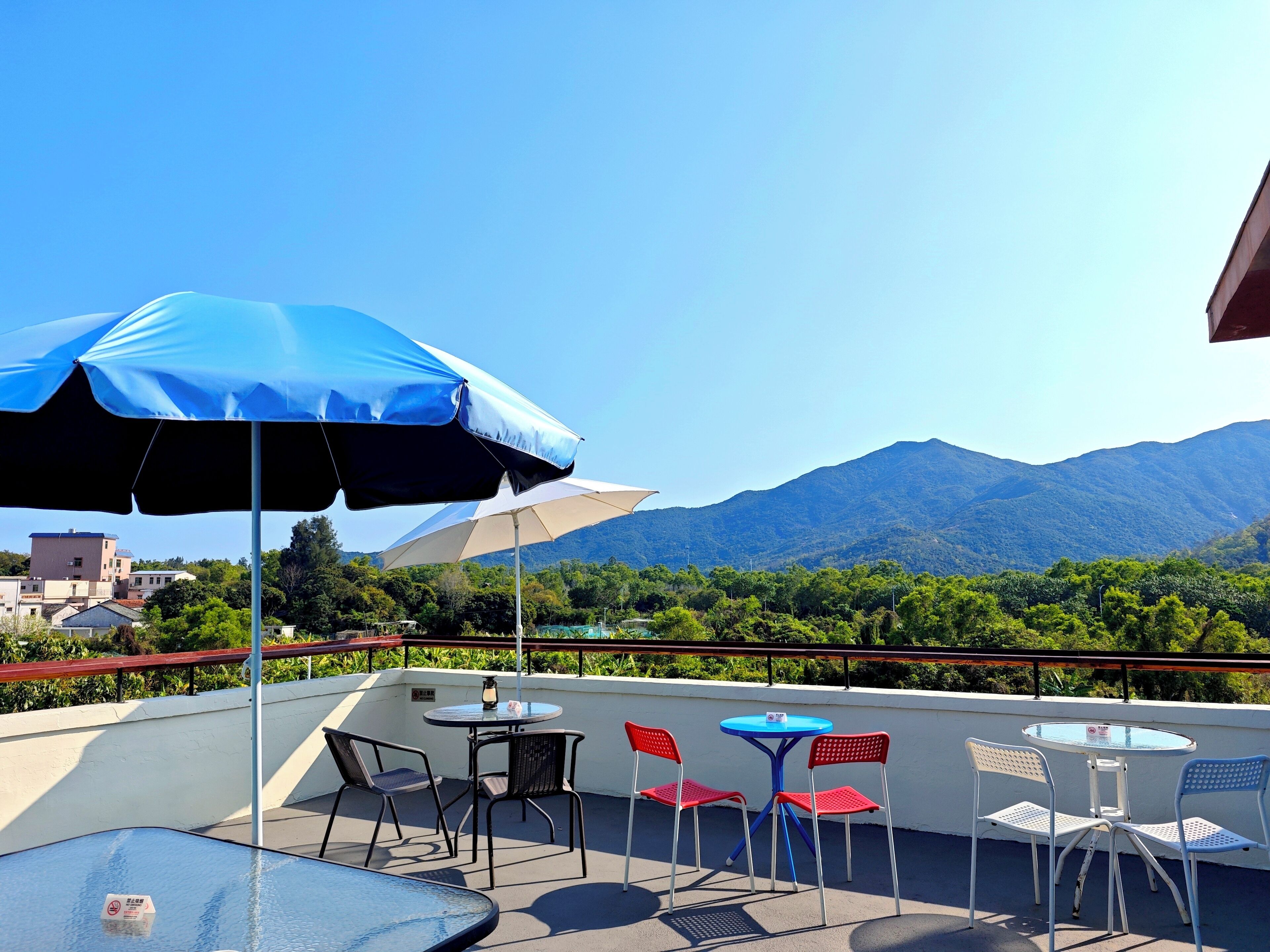 A terrace with a table and chairs, a blue umbrella, and a mountain view.