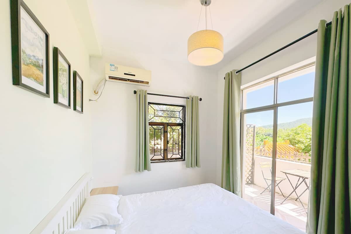 Une chambre à coucher avec un lit, une fenêtre avec des rideaux, un luminaire au plafond et un climatiseur fixé au mur.