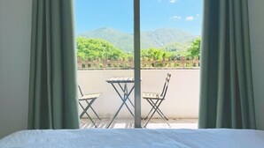 Une chambre avec un lit, une fenêtre avec des rideaux et une vue sur une montagne et la verdure.