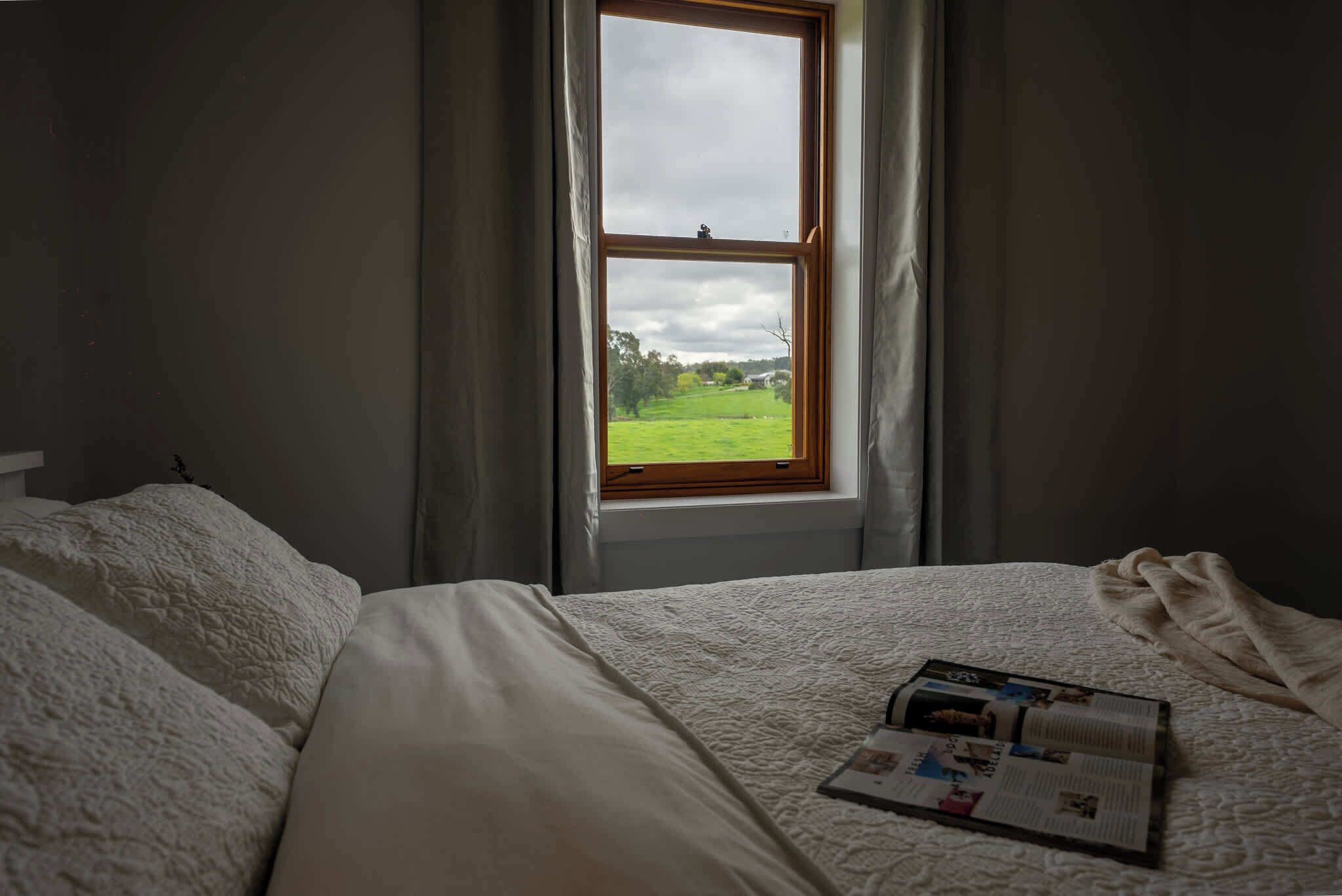 Una camera da letto con una grande finestra, un letto con lenzuola bianche e una rivista sul letto.