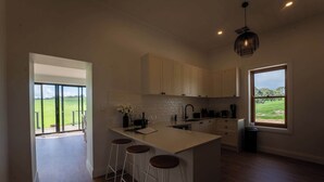 Uma cozinha moderna com uma ilha grande, banquetas e vista para um campo verde pela janela.
