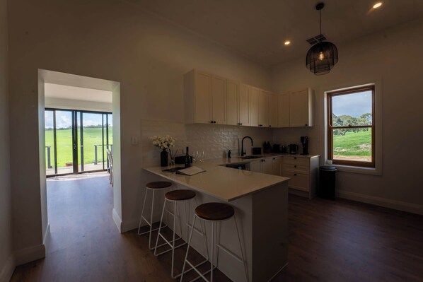 Eine moderne Küche mit einer großen Kochinsel, Barhocker und Blick auf ein grünes Feld durch das Fenster.